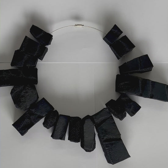 A video of a close up of a large rectangular shaped choker of black rubber