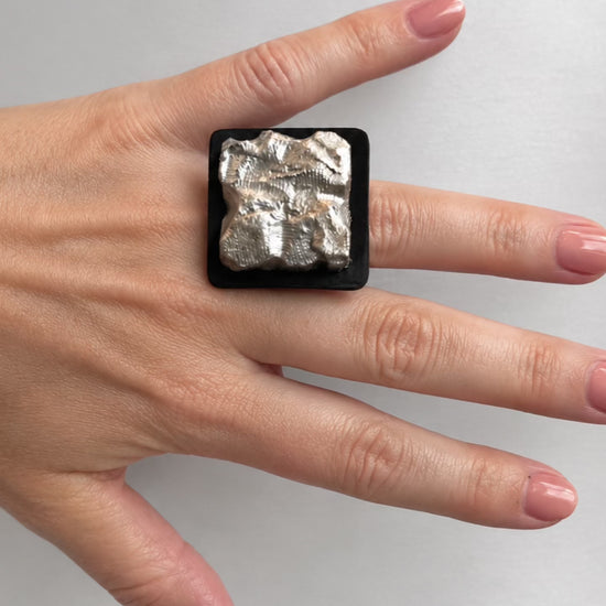 A video of a hand wearing a black and silver square ring
