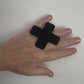 A hand wears a large cross shaped black ring