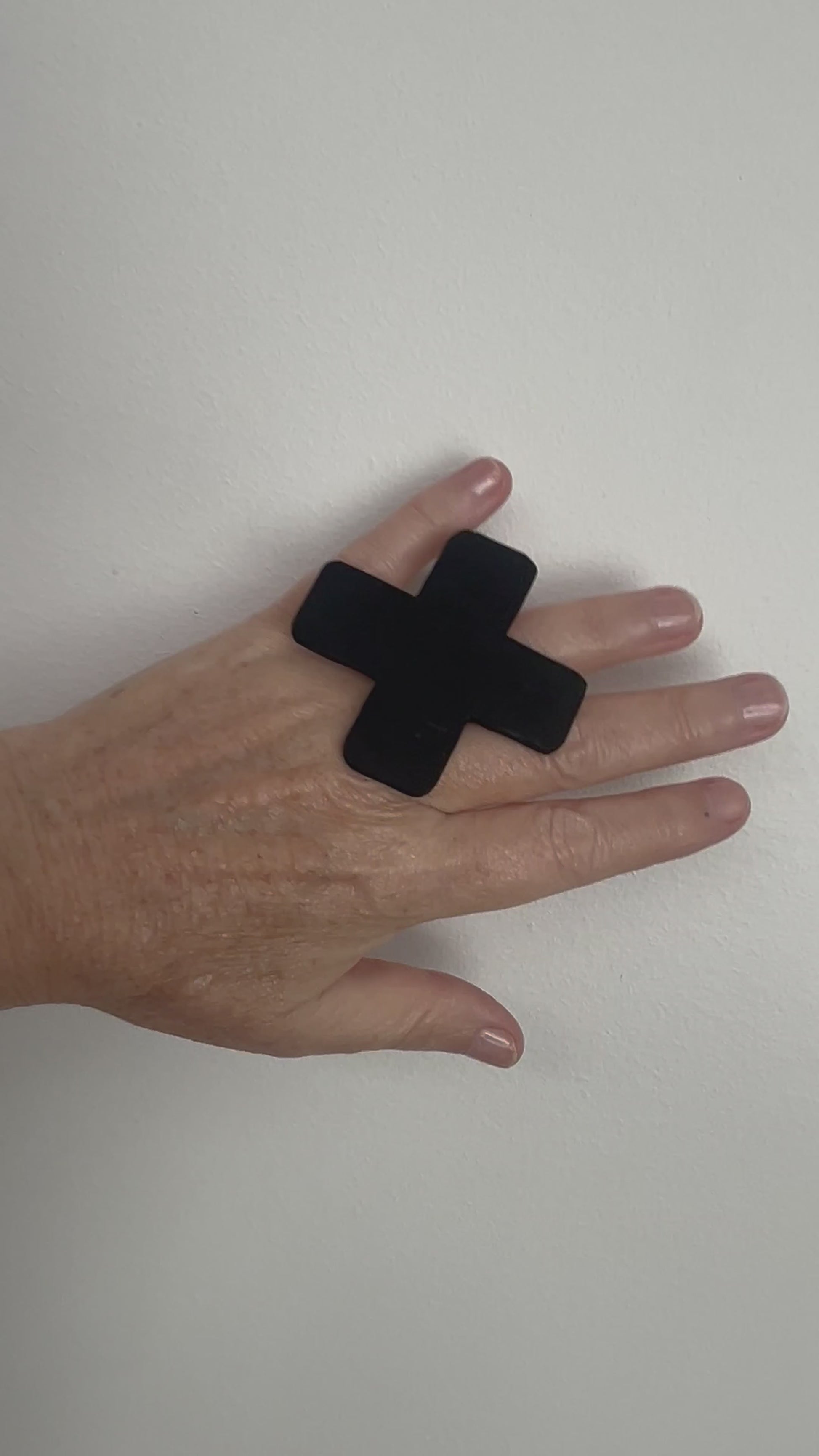 A hand wears a large cross shaped black ring