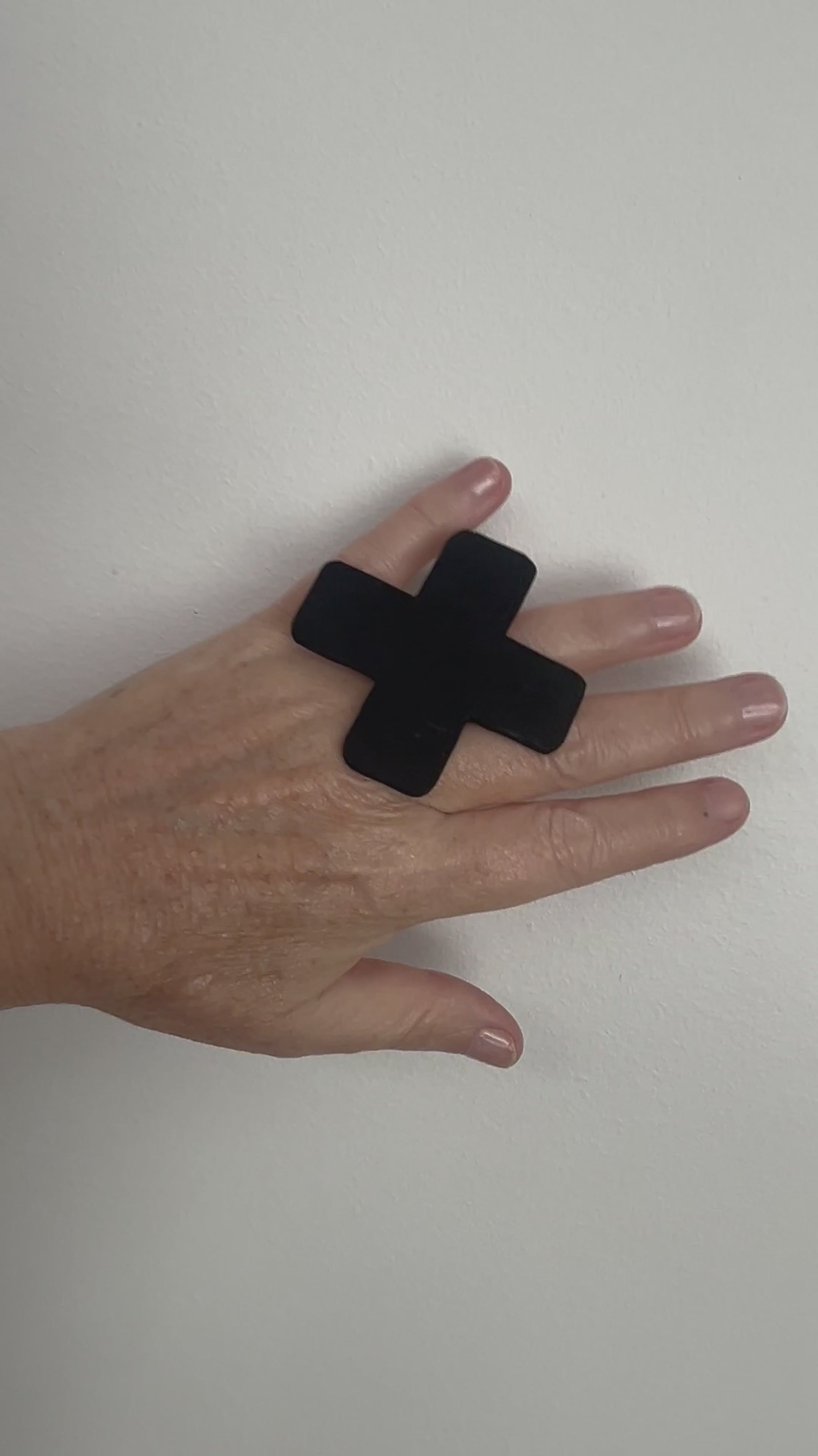 A hand wears a large cross shaped black ring