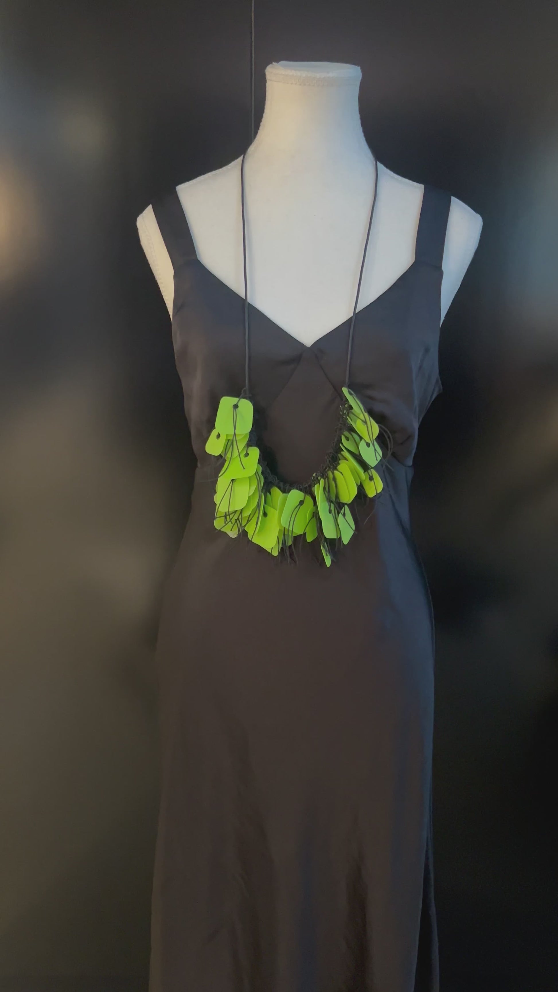 A hand plays with a necklace made from green coloured recycled plastic