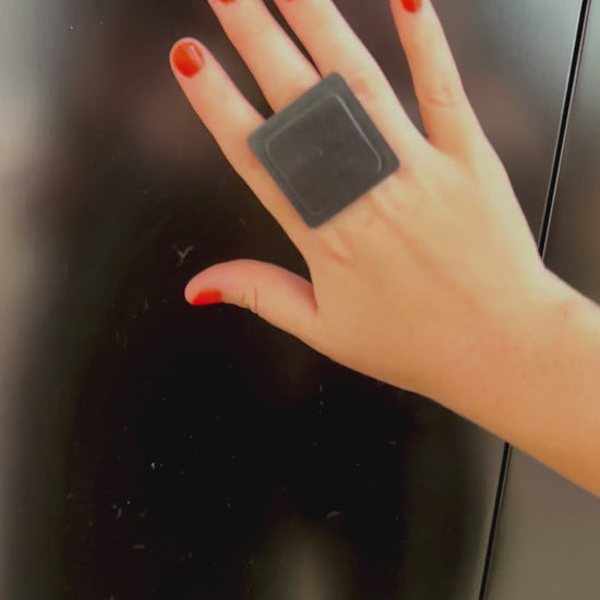 A woman wears a large square black ring made from repurposed rubber