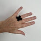 A woman's hand wears a small cross shaped black ring