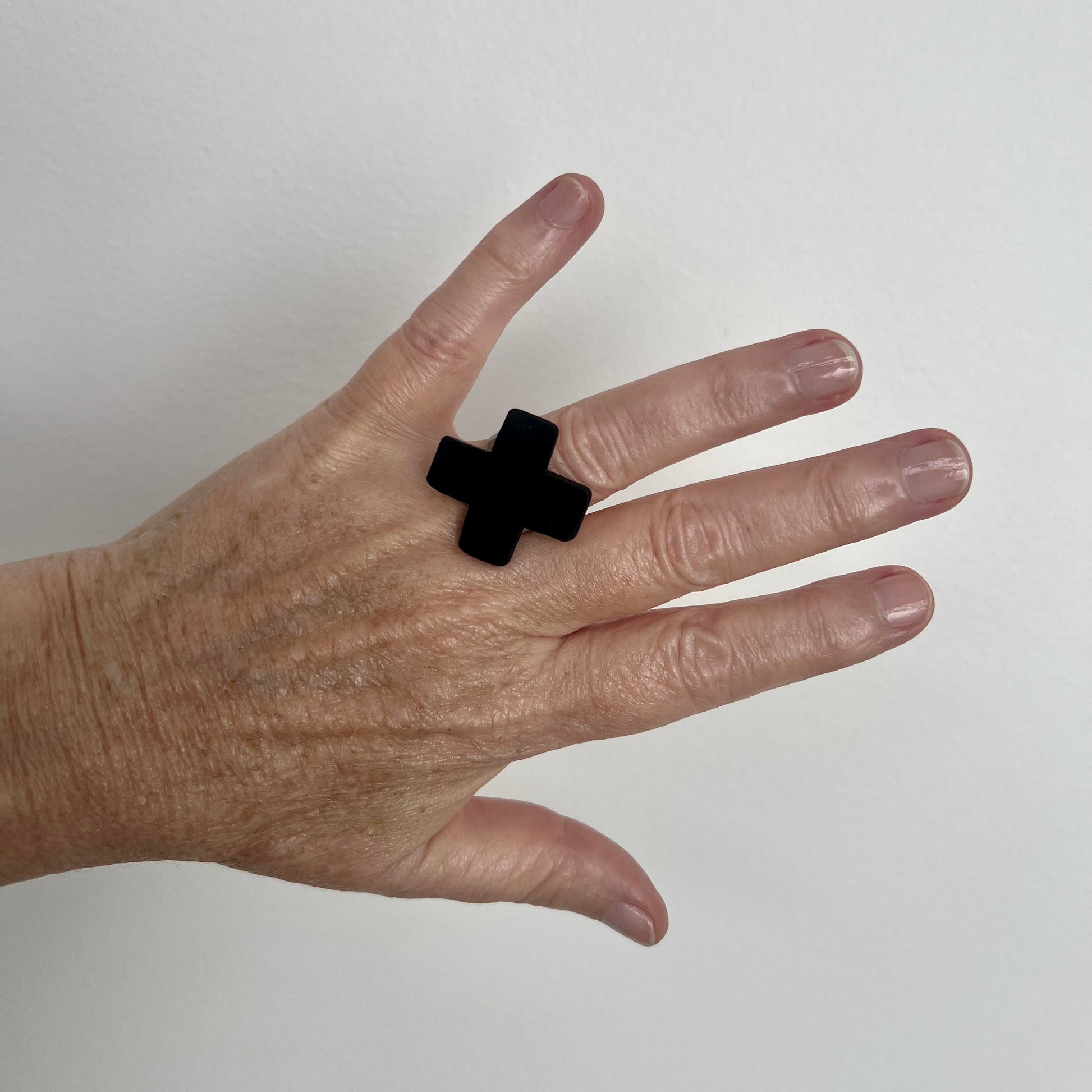 A woman's hand wears a small cross shaped black ring
